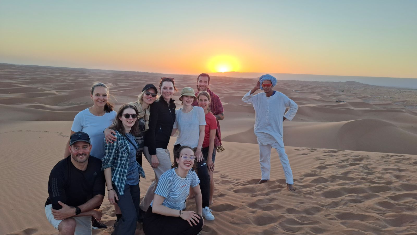 Group of tourists posing on Sahara sand dunes at sunset