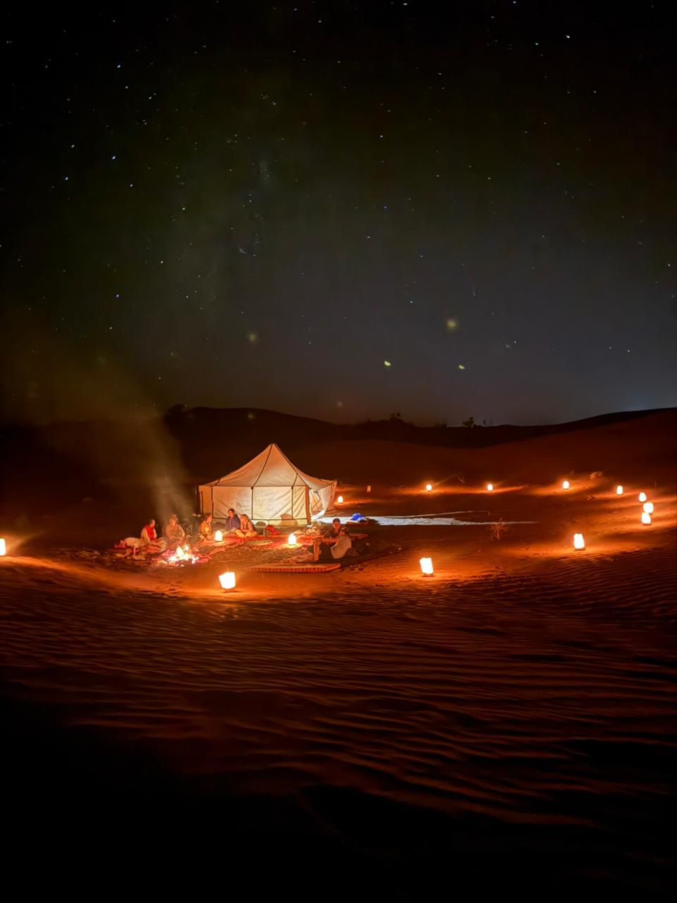 Desert camp illuminated by lanterns under a starry night sky